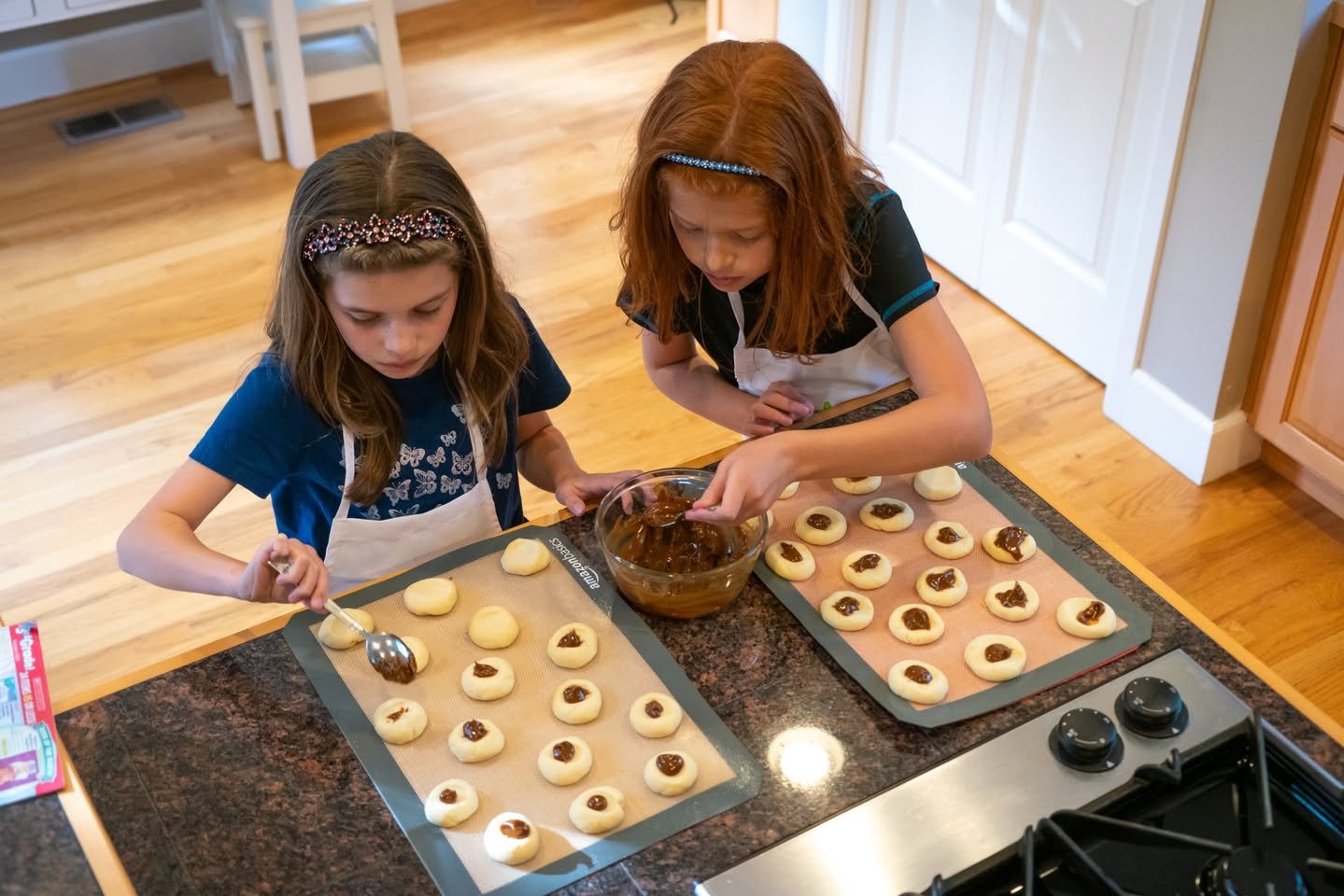 Junior Chefs Two children wearing aprons filling cookie dough on baking sheets.