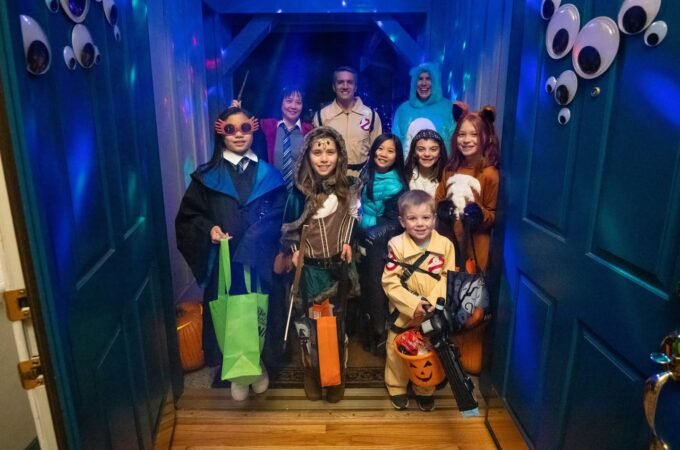 A group of costumed people posing in a vividly lit, eye-covered entrance hallway during a themed event. Colorful bags and costumes suggest a fun, family-oriented experience.