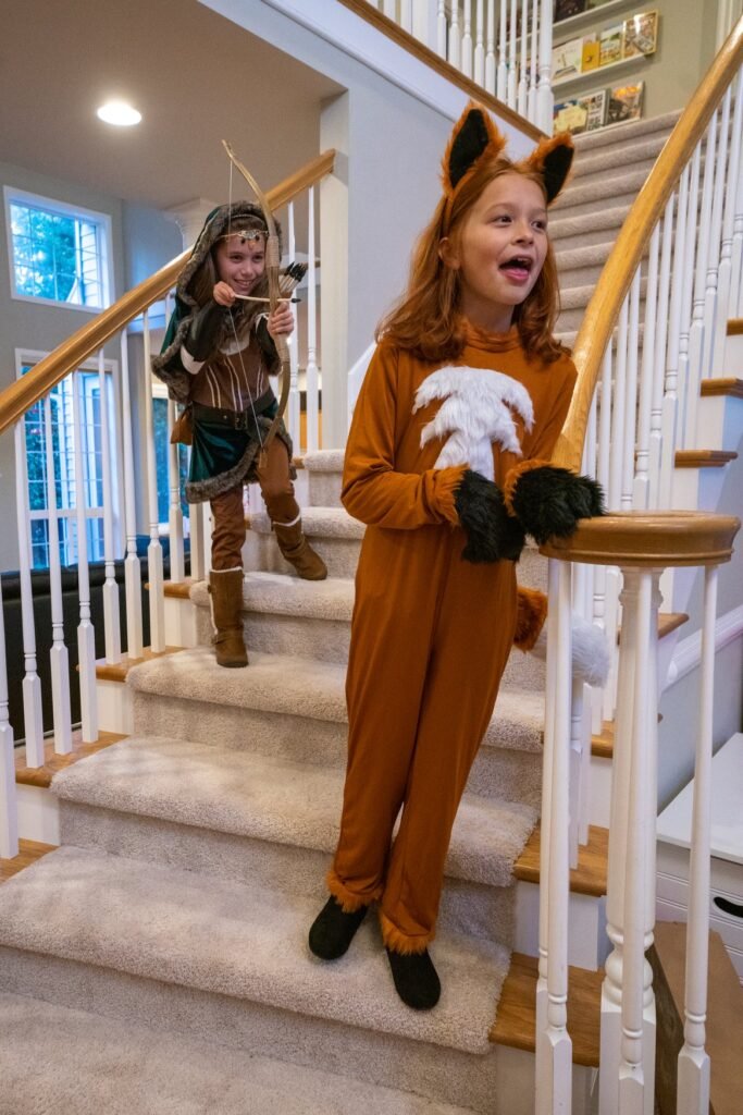 Kids in Fox and Robin Hood costumes play on a carpeted staircase.
