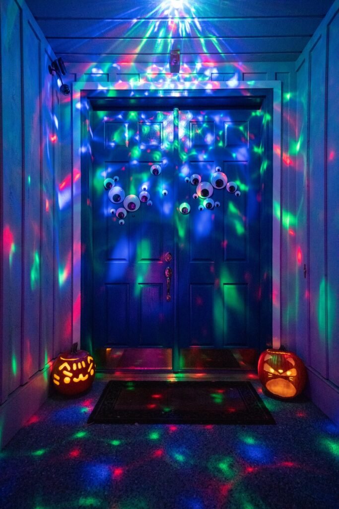 Colorful laser lights shine across a front porch, illuminating a front door and two glowing jack-o'-lanterns in a festive Halloween display.