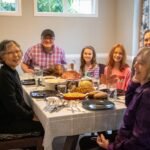 A group of seven people enjoying a shared meal around a dining table in a bright room.