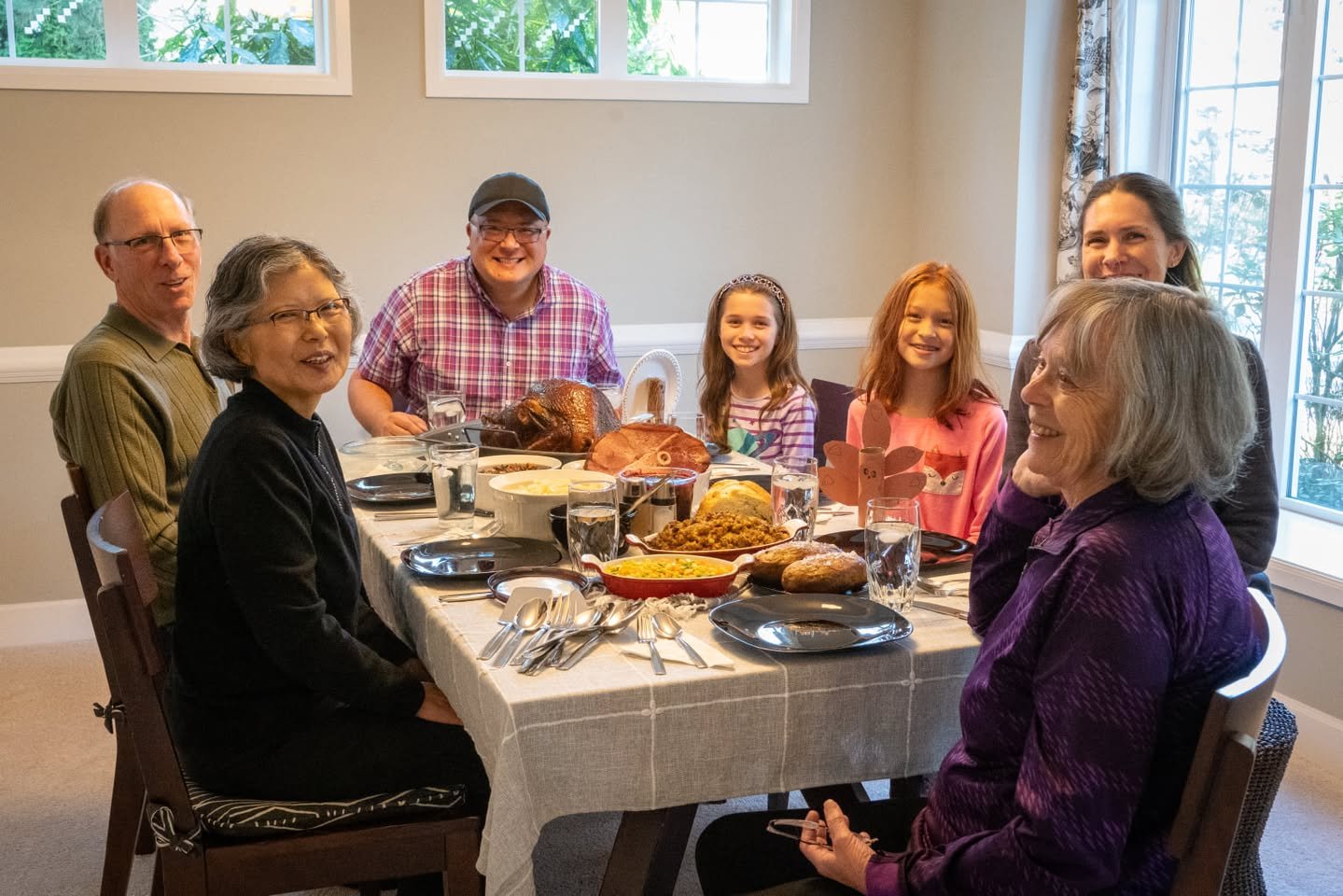 A group of seven people enjoying a shared meal around a dining table in a bright room.
