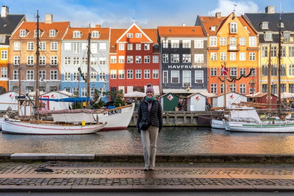 A person walking along the cobblestone quay of Nyhavn in Copenhagen, Denmark, with historic colorful buildings and boats.