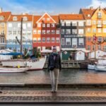 Christmas Piano Recital A person walking along the cobblestone quay of Nyhavn in Copenhagen, Denmark, with historic colorful buildings and boats.