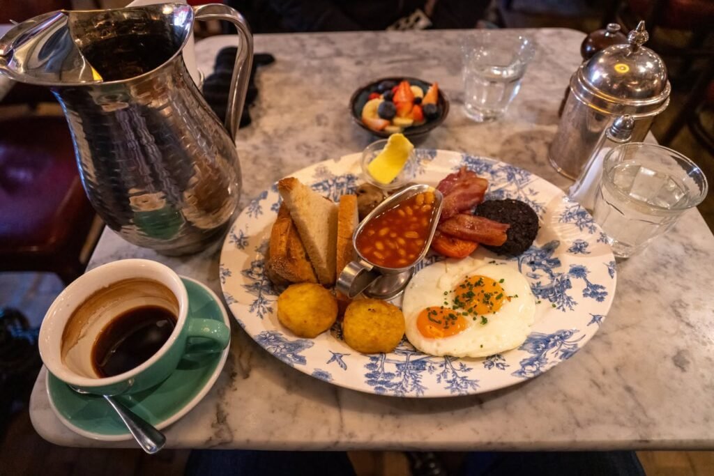 A hearty breakfast plate with eggs, toast, and condiments served with a cup of tea. A silver pitcher and glass canisters complete the table setting.