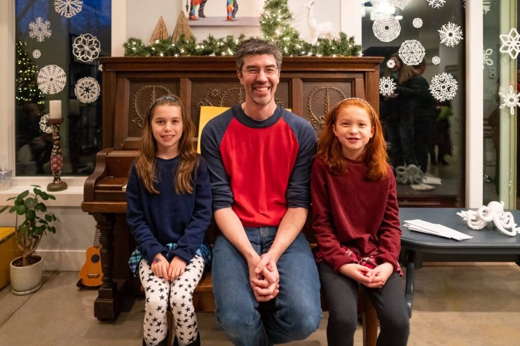 Family photo in front of a wooden organ with painted snowflakes on the window behind them.