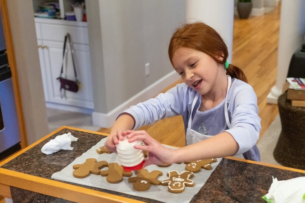 A child decorates gingerbread cookies on a kitchen counter, using a shaker to add icing.