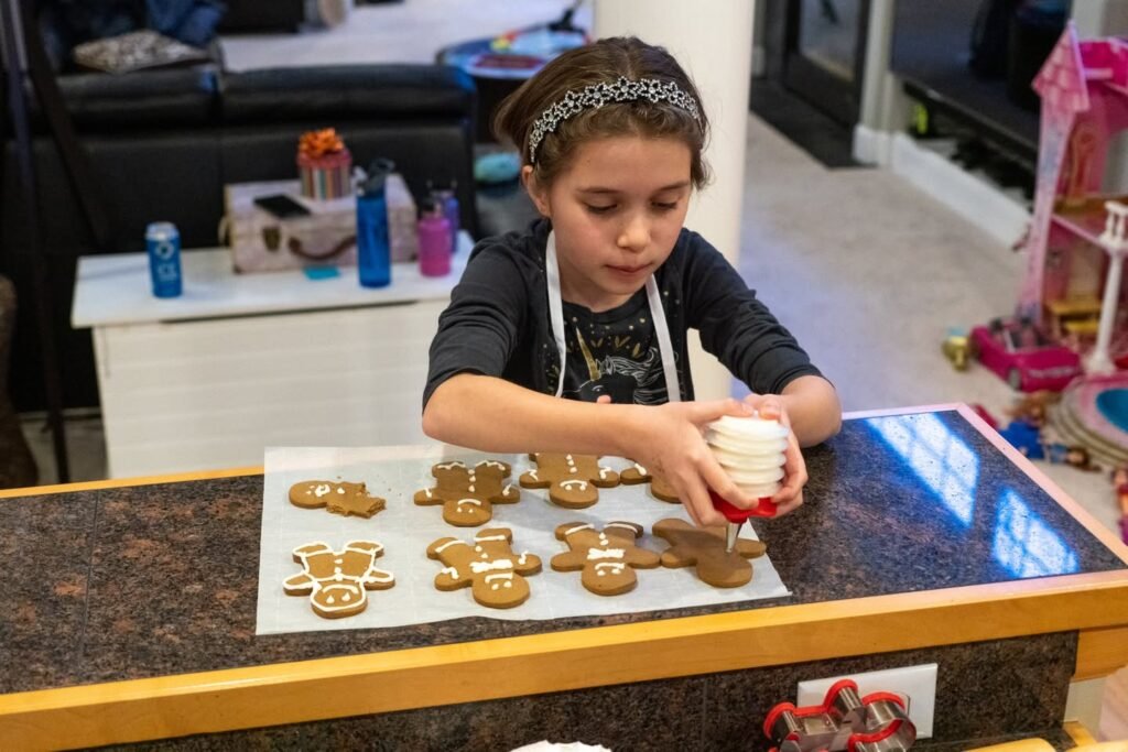 A child wearing an apron decorates gingerbread man cookies on a kitchen counter.