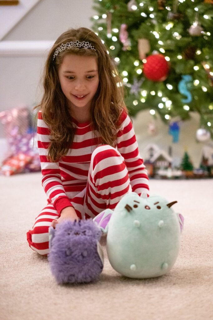 A child in red striped pajamas playing with Sumikko Gurashi sumi peluche toys by a Christmas tree.