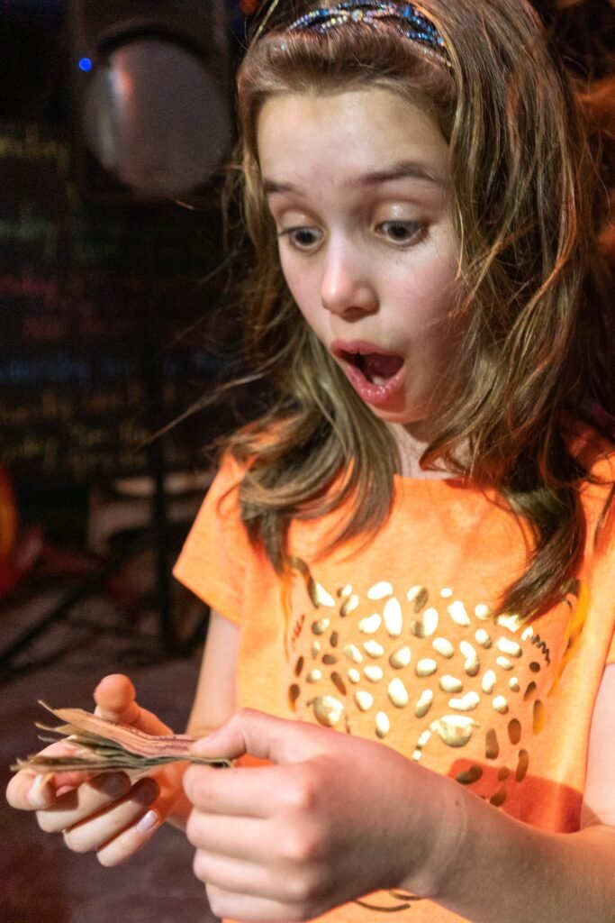 A person in an orange shirt holds a bundle of wooden sticks with a surprised expression.