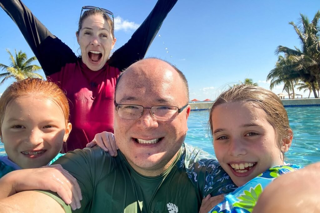 Family members having fun at a pool in a tropical setting, laughing and enjoying the bright and sunny day.