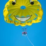 Belize Day 3 A yellow paraglider canopy with a painted smiley face design floats against a bright blue sky.