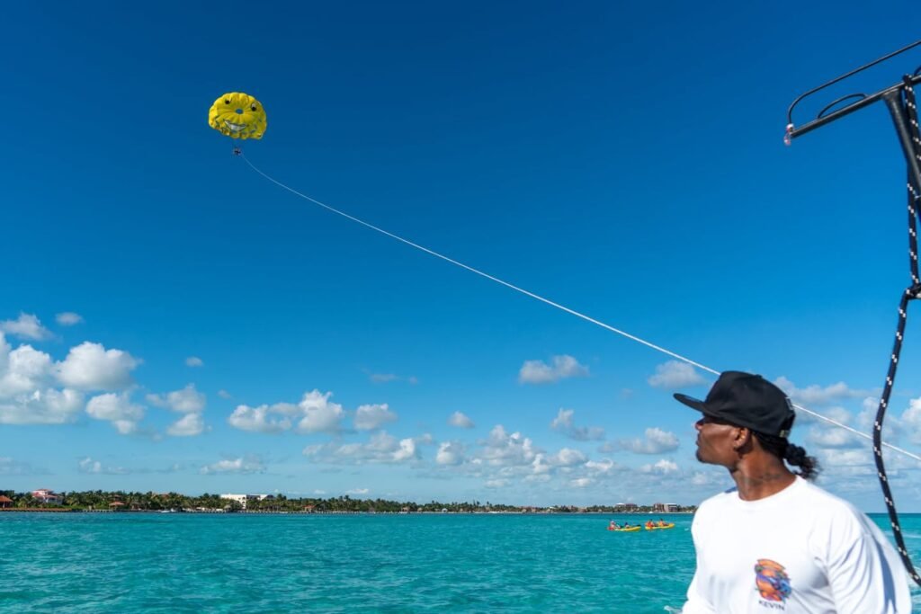 A person stands on a boat holding a parasailing line under a bright blue sky, with vibrant turquoise water stretching to the horizon.