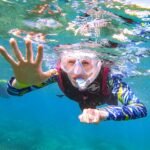 An underwater snapshot of someone skin diving in clear, blue-green water while wearing snorkeling gear.