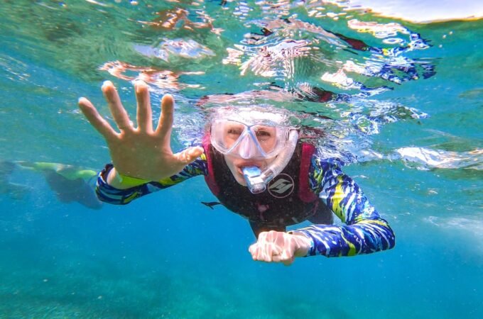 An underwater snapshot of someone skin diving in clear, blue-green water while wearing snorkeling gear.