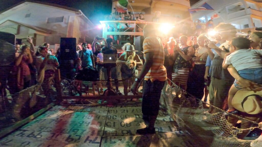 A lively crowd gathers at a nighttime rooftop party with string lights and festival decorations.
