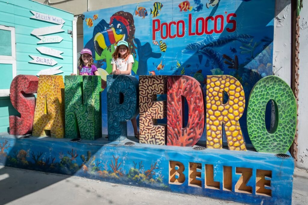 A vibrant mosaic sign spelling San Pedro, Belize with people posing against a lively mural background at Poco Loco's.