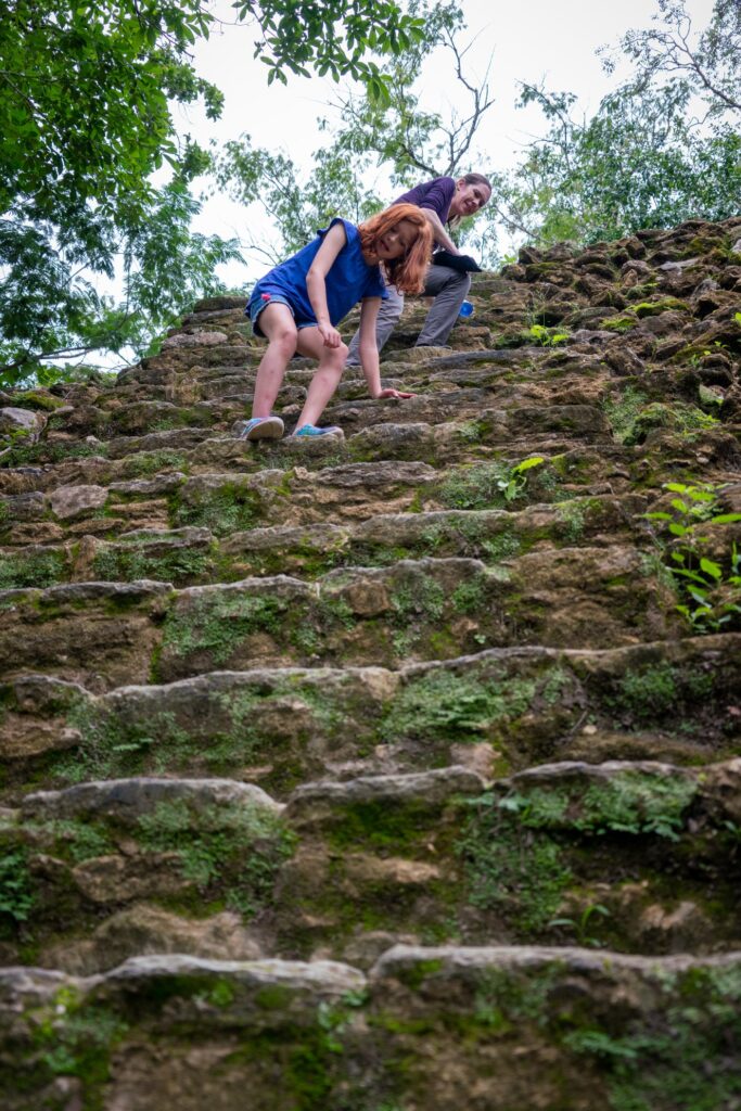 Exploring ancient moss-covered stone steps surrounded by dense forest foliage. Two hikers climbing a historic staircase.