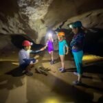 Belize Day 8 A group wearing helmets and headlamps explores a lit cave interior.