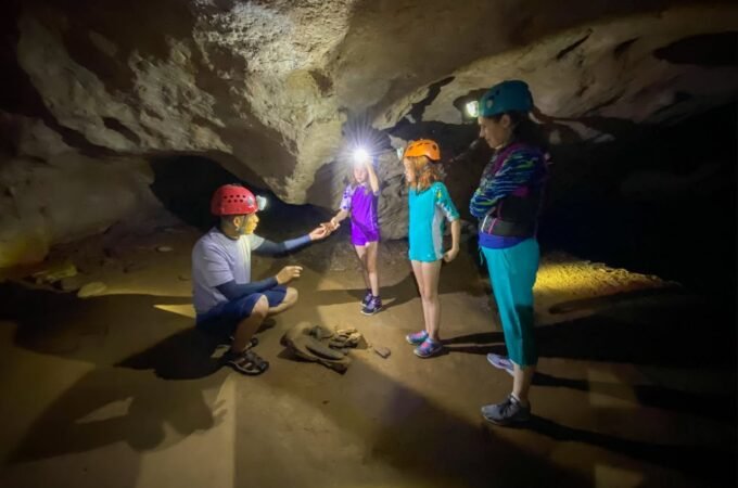 A group wearing helmets and headlamps explores a lit cave interior.