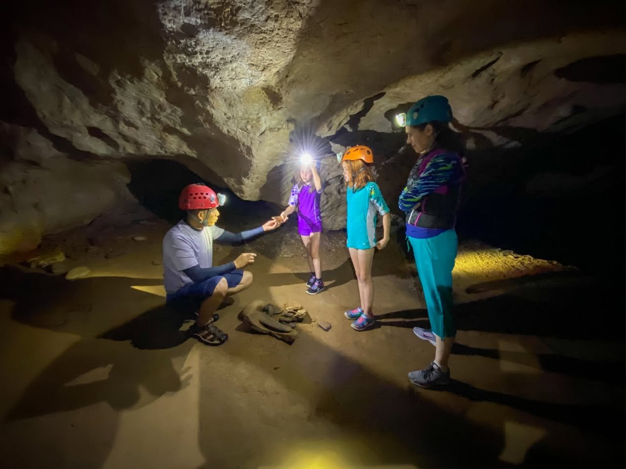 Belize Day 7 A group wearing helmets and headlamps explores a lit cave interior.