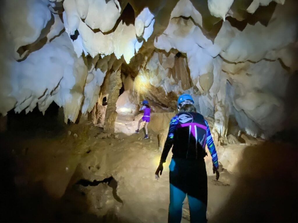 Individuals wearing headlamps explore a cavern with intricate rock formations.