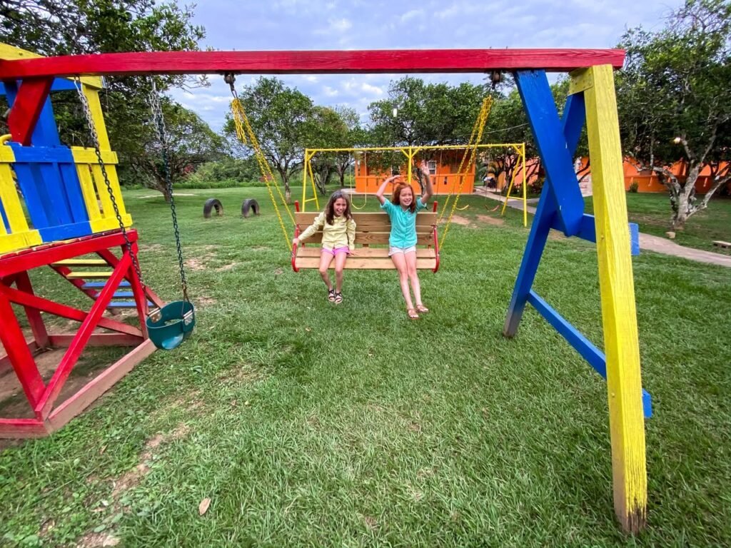 People enjoying a colorful swing set in a vibrant green park setting.