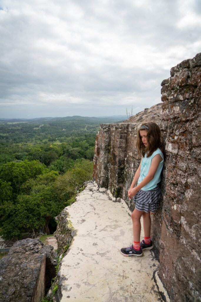 A person stands near a stone structure at Chichen Itza, overlooking an endless canopy of dense green forest.
