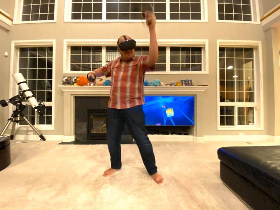 Person playing a virtual reality game at home. Living room features a TV, telescope, and cozy carpets.