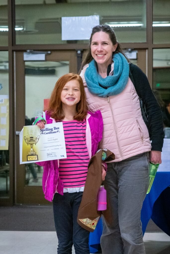 Two individuals posing with an award certificate outside a building entrance.