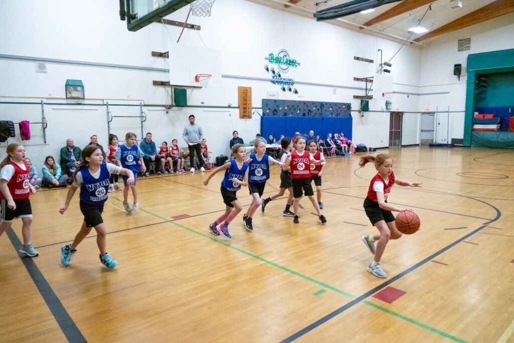 Young players compete in a basketball game while spectators watch from the sidelines.
