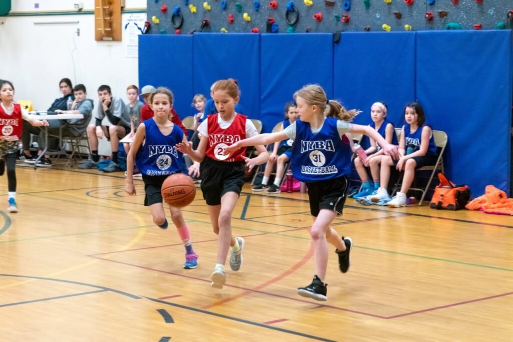 Young basketball players in action on a gymnasium court during a game, with spectators watching. The scene captures the energy and excitement of youth sports in a Pacific Northwest community.
