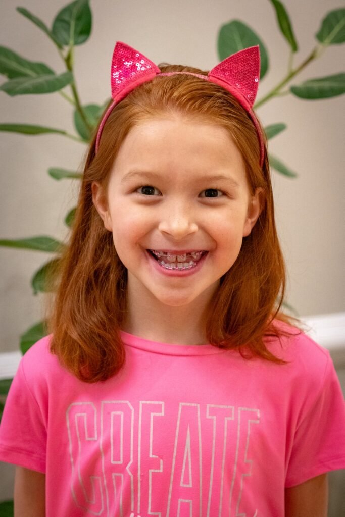 A smiling child wearing a pink t-shirt with the word 'CREATE' on it and pink glittery cat ears.
