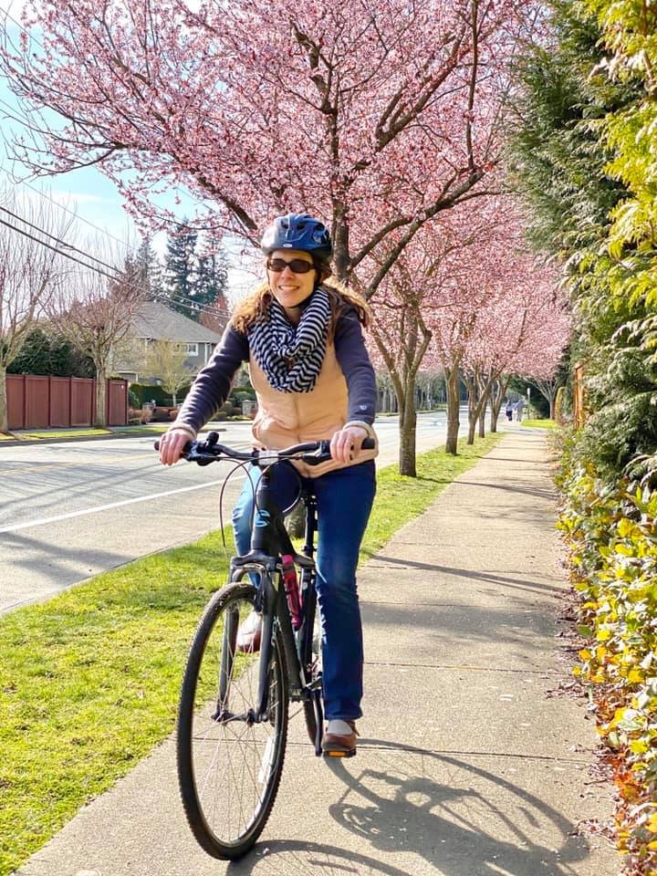 A person enjoys a bike ride on a sidewalk bordered by cherry blossom trees in full bloom.