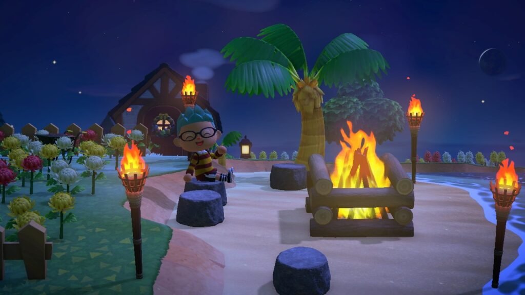 A screenshot from Animal Crossing showing a character sitting at a campfire on a beach at night surrounded by torches and flowers.