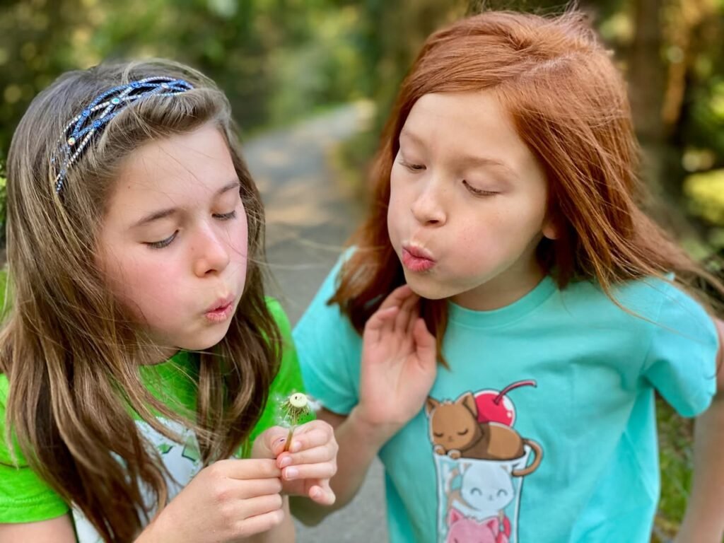 Two young girls examining a small flower and playing outdoors on a sunny day in the Pacific Northwest.