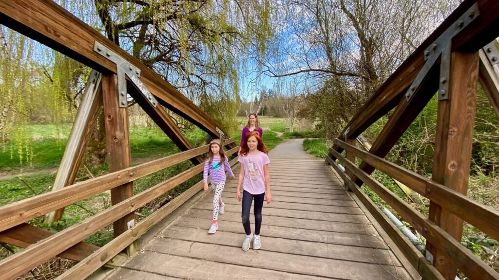 Children walking across a wooden park bridge in a green landscape. A rustic structure in the Pacific Northwest.