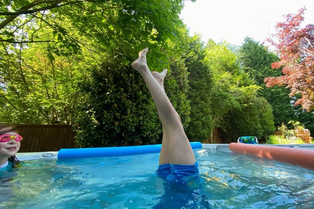 Enjoying a sunny day in a backyard swimming pool surrounded by lush green trees and leaves.