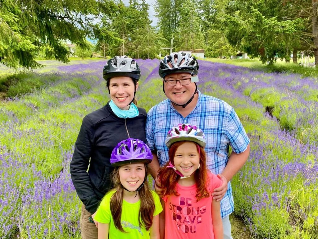 A family wearing bicycle helmets enjoys a cycling day in a vivid lavender field with lush green trees.