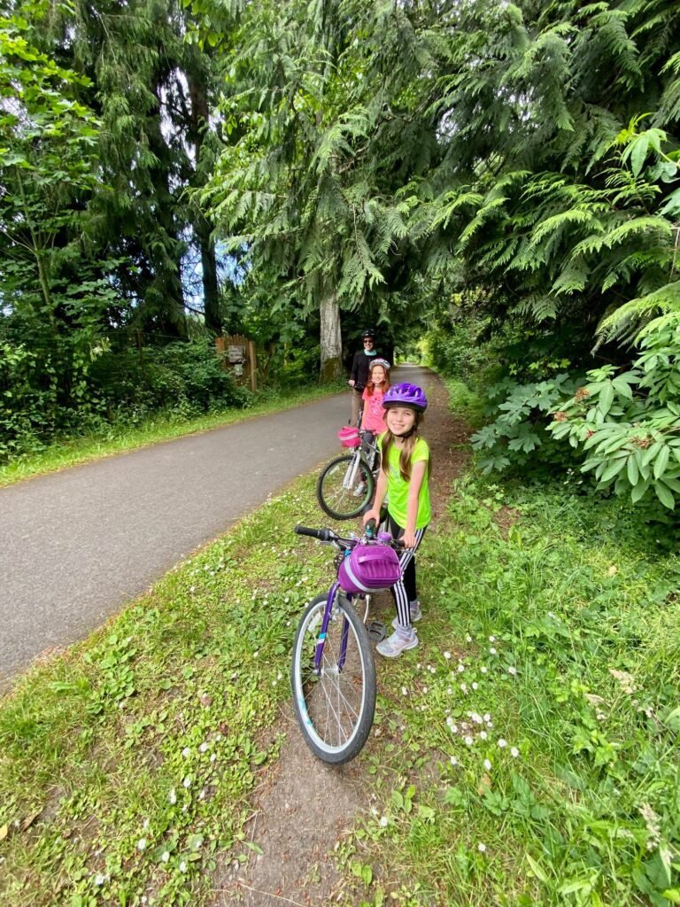 A child in a purple helmet with a purple bicycle on a grassy trail.