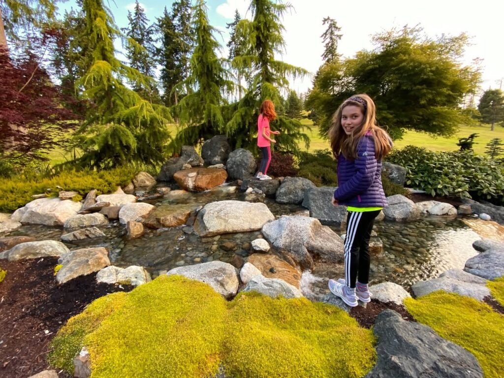 A serene Japanese garden with moss and rocks, with two people standing among the greenery, capturing a quiet moment in nature.
