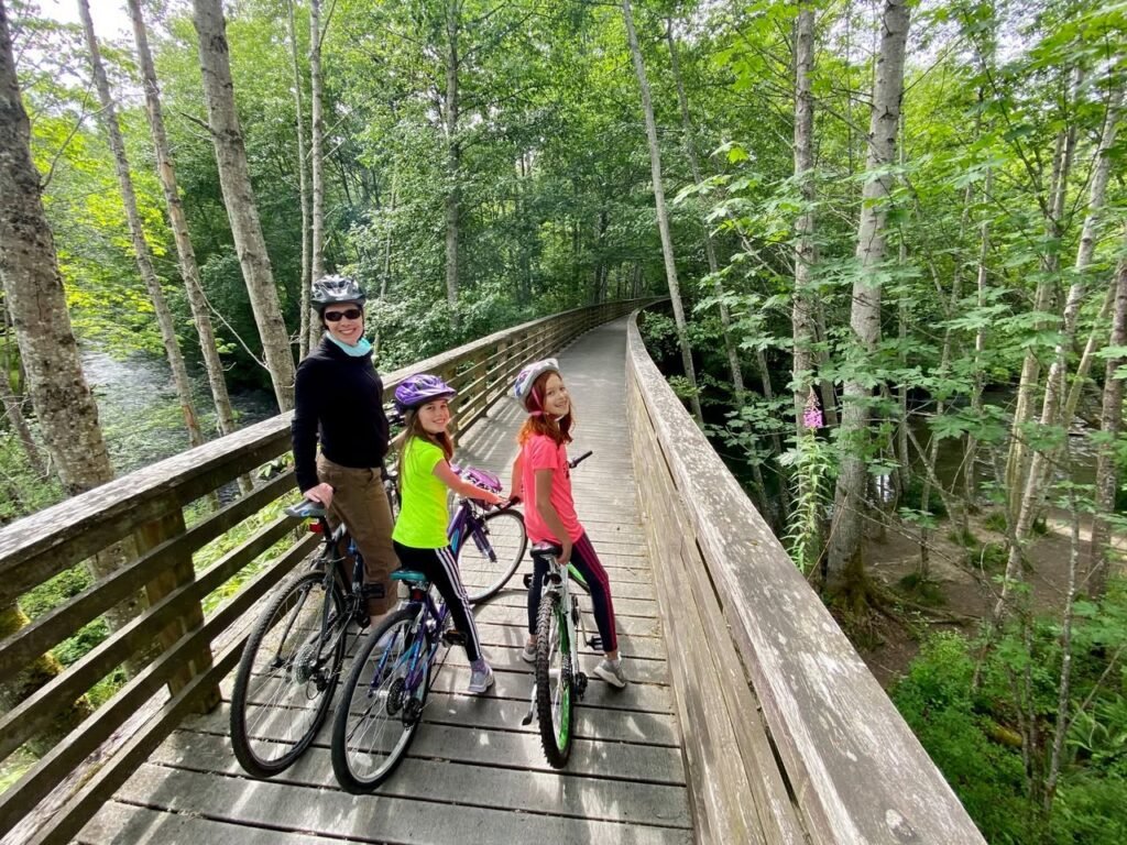 A group riding bicycles on a wooden bridge through a lush green forest in the Pacific Northwest.