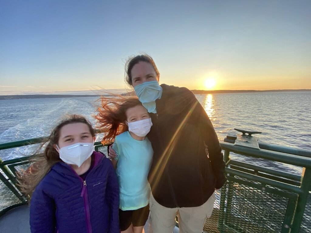 A selfie of passengers wearing masks on a boat deck as the sun sets over the water. Capturing a family moment during a cruise on the Pacific Northwest waterfront.