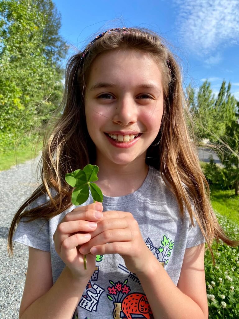 A joyful moment capturing a child holding a four-leaf clover outdoors on a sunny day.