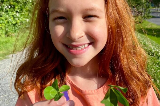 A young child is holding a small branch of vibrant red leaves outdoors on a sunny day.