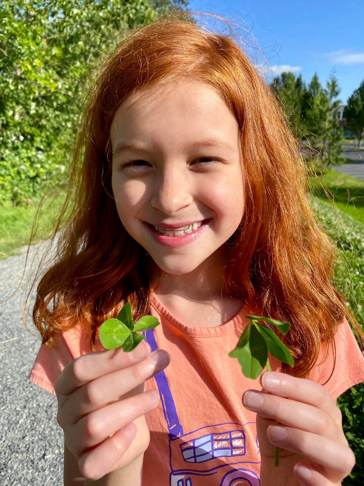 Lucky A young child is holding a small branch of vibrant red leaves outdoors on a sunny day.