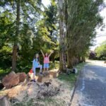 Two children play on large rocks beside a gravel trail in a lush forest setting, captured in the Pacific Northwest.