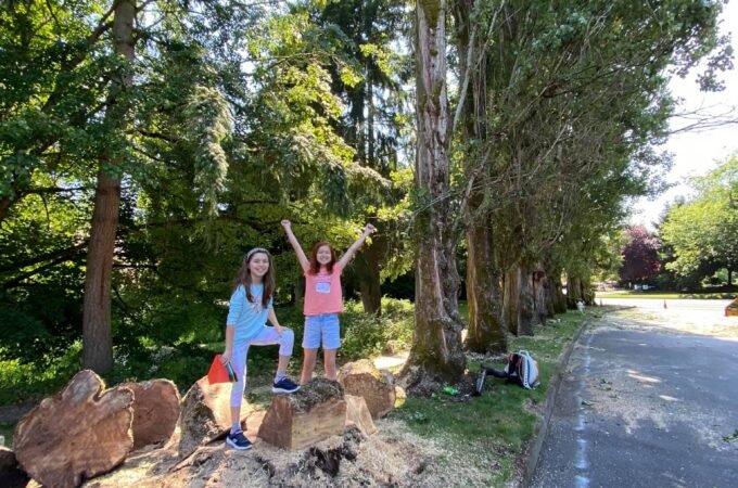 Two children play on large rocks beside a gravel trail in a lush forest setting, captured in the Pacific Northwest.