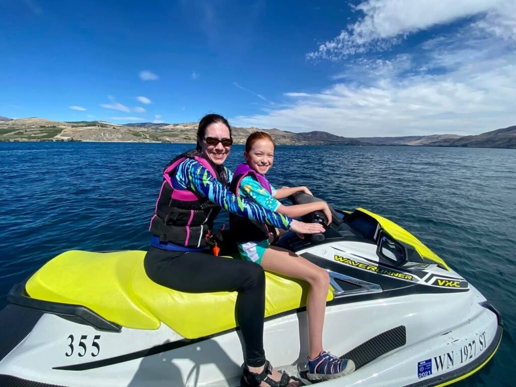 Two people riding a jet ski on a lake under a clear blue sky. Detailed shots of the jet ski and surrounding water.