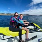 Two people riding a jet ski on a lake under a clear blue sky. Detailed shots of the jet ski and surrounding water.